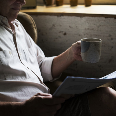 photo of a man reading paper and holding a mug